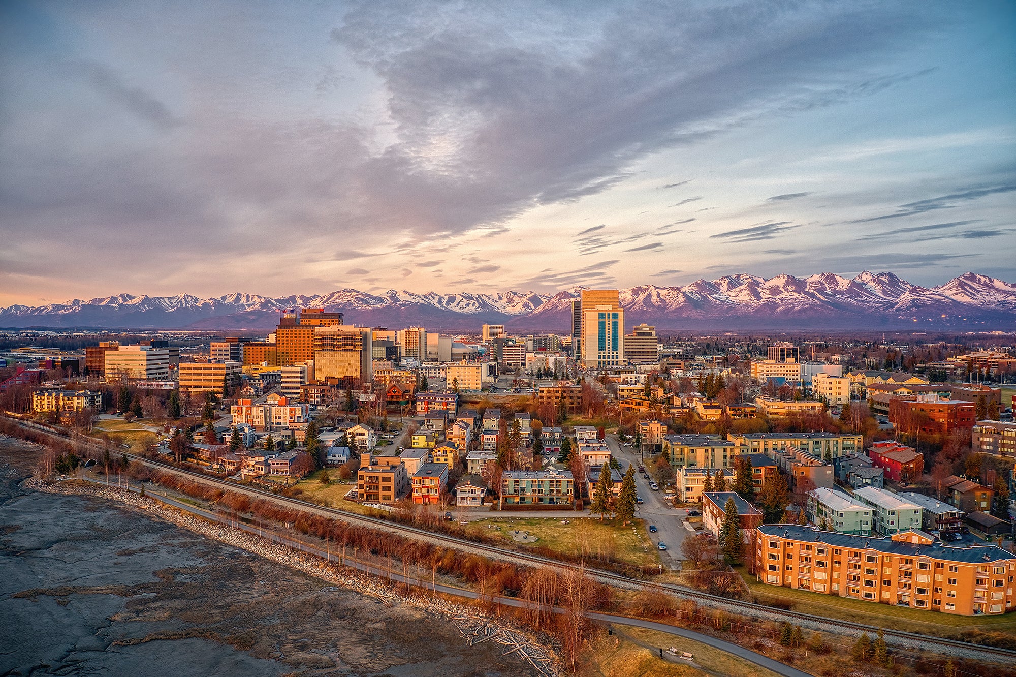 Downtown Anchorage An areal photo of Anchorage, a medium sized city, in the foreground, with snowy mountains in the distance.