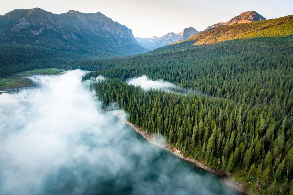 A drone photo created while flying over Hyalite Reservoir in the Gallatin Mountains of Montana. The sun is just beginning to rise and fog covers much of the lake.