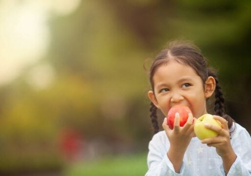 Close-up of girl eating apples near trees.